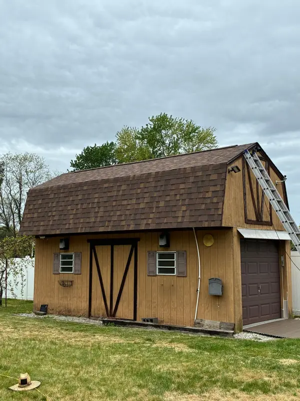 Barn-style shed with new brown shingles and a ladder at the eave