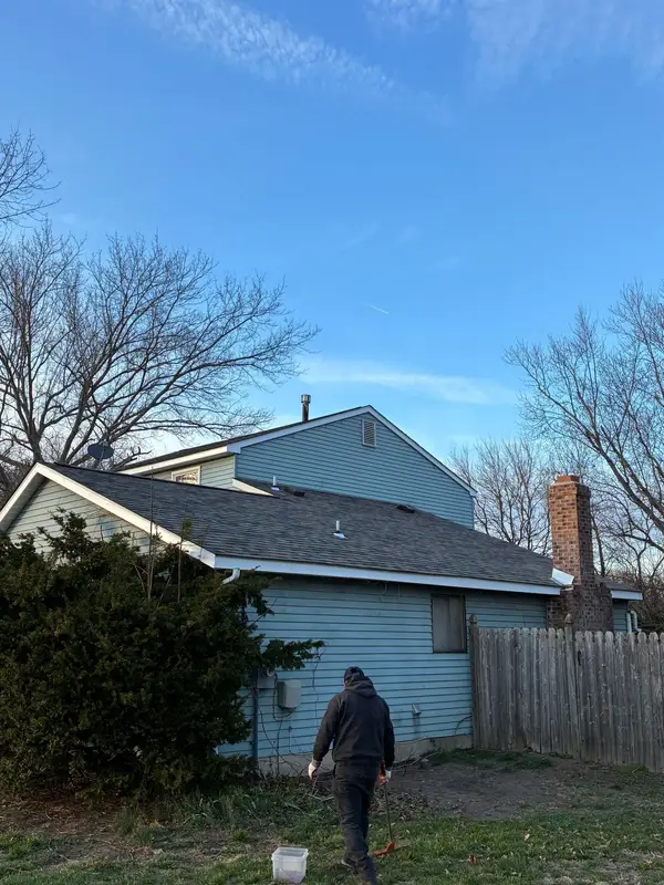 Crew member cleaning up the yard beside a blue home with a finished roof