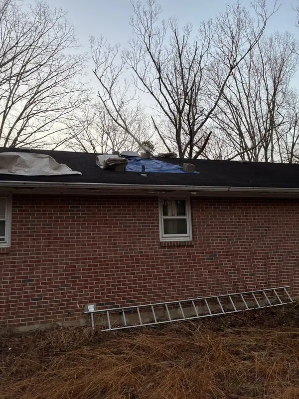 Brick ranch home with old shingles partly stripped and a ladder in the yard