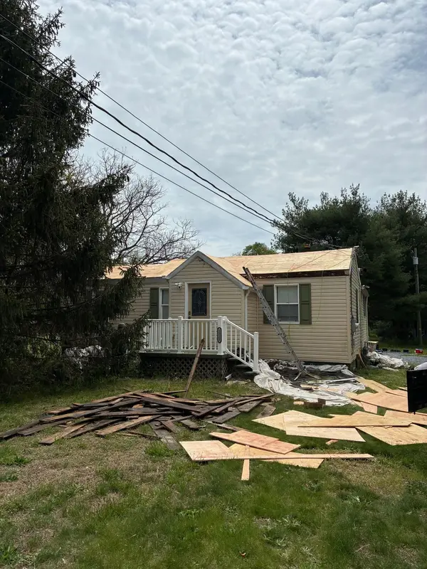 Small Cape Cod home with new plywood roof decking and the old roof boards piled on the lawn