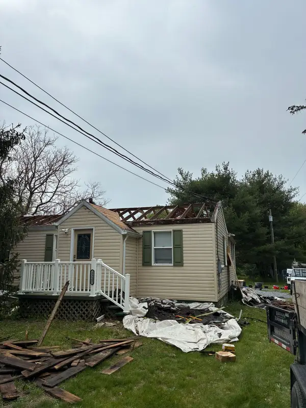 Cape Cod home with its roof stripped to the rafters and tarps catching debris