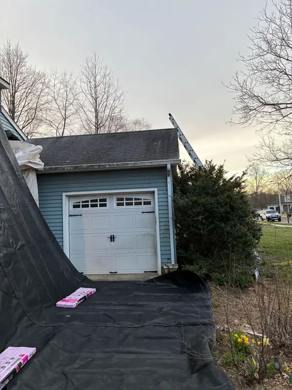 Garage with a new gray shingle roof and protective tarps on the driveway
