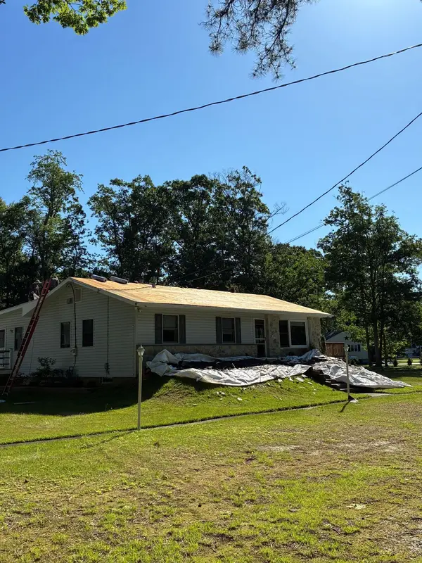 Tan ranch home mid tear-off with tarps protecting the lawn and a ladder at the eave