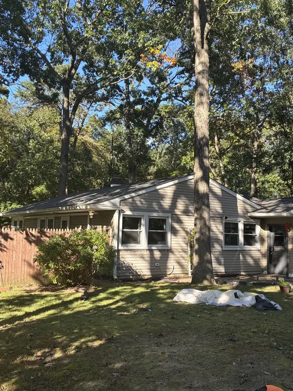 The same tan ranch home after the job, shaded by tall trees