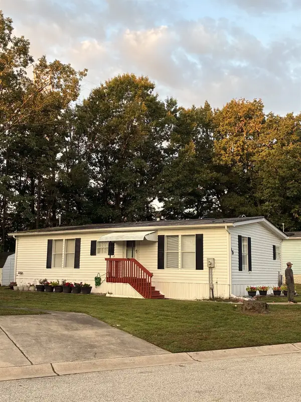 White manufactured home with black shutters and red front steps at sunset