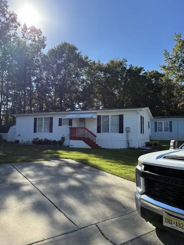 The same white manufactured home on a sunny day, with a work truck in the driveway