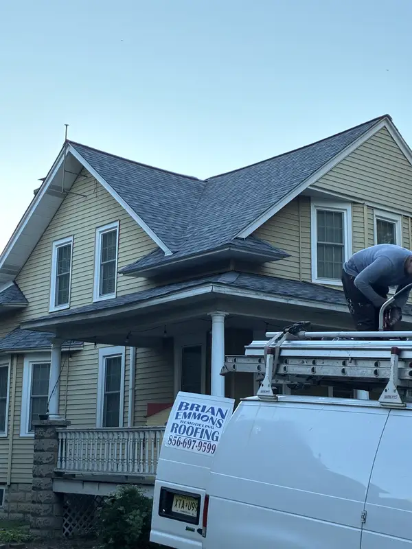 The same yellow home with a new gray architectural shingle roof and a Brian Emmons Roofing van out front